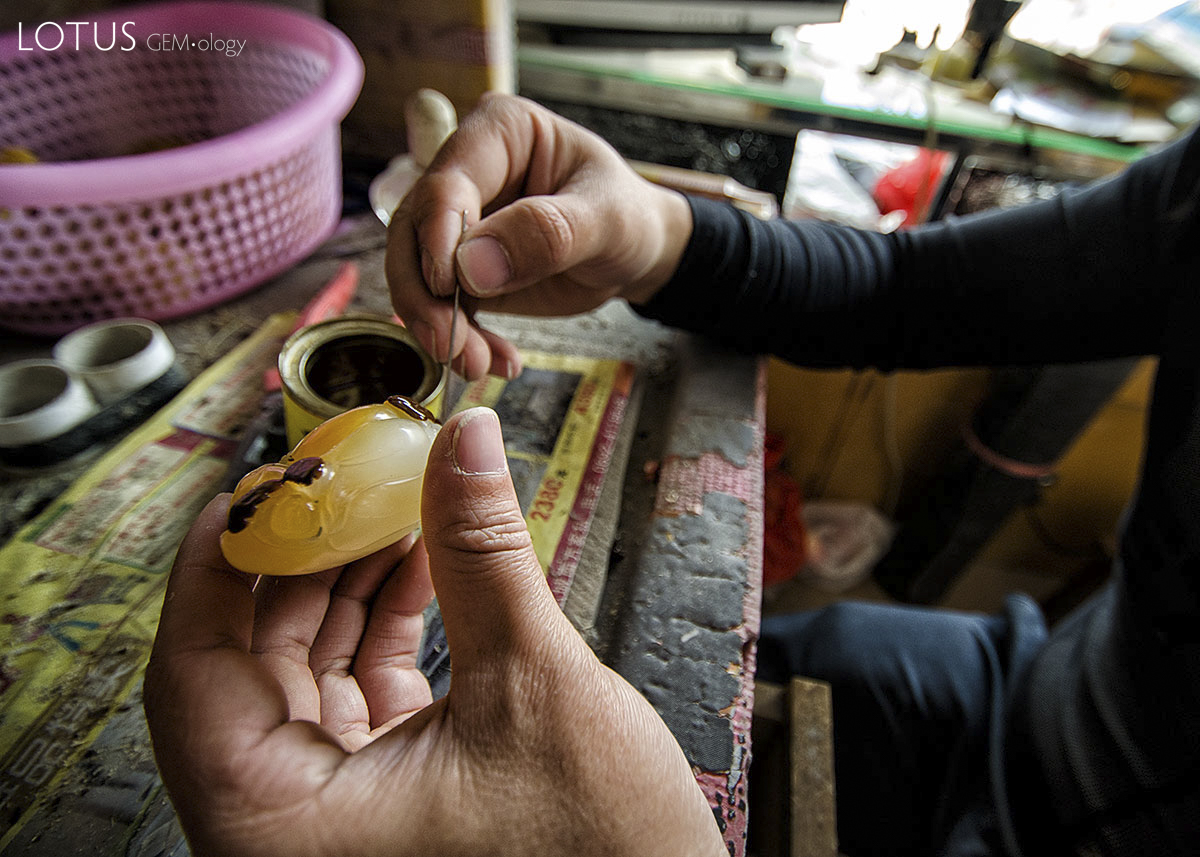Figure 14. Applying a reddish varnish to the surface of a jade-like material in a workshop in Ruili's jade market (top). Following the treatment, which probably involves firing in an oven, the treated portions assume a reddish color that simulates the natural oxidation staining on the surface of jade boulders. Photo: Richard W. Hughes.