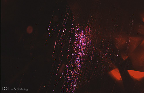 Figure 4. Fiber-optic illumination reveals the rain-like stringers of flux particles in the Kashan ruby that are so typical of this type of synthetic. Magnified 15&times;. Photomicrograph &copy; John I. Koivula, microWorld of Gems.