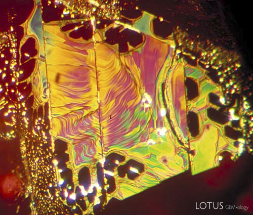 Figure 4.  &hellip;equals internal symmetry Secondary fluid inclusions (healed fractures, or &lsquo;fingerprints&rsquo;) often display the symmetry of the underlying crystal structure in the healed areas. Above is shown a healed fracture in a Thai ruby which formed parallel to the basal pinacoid. As the c axis (3-fold symmetry) runs perpendicular to this face, the healed (dark) areas display distorted hexagonal or triangular (60/120&deg;) outlines. Vertical lines cutting through the fingerprint are repeated twinning striations. Photo &copy; Richard W. Hughes