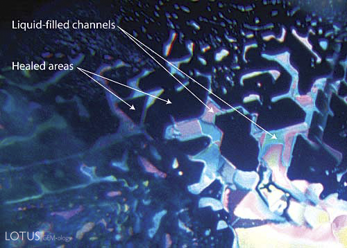 Figure 1. Anatomy of a healed fracture A well-healed fracture in a sapphire lying roughly parallel to the basal plane. The healed areas appear dark, while the undigested fluids are highly reflective. Note that the pattern of healing relates to the underlying crystal structure, with angles of healed areas following the underlying crystallographic structure (in this case, at 60/120&deg;). Photo &copy; Richard W. Hughes