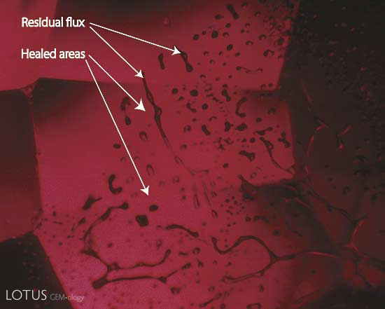 Figure 6. Flux-healed fracture Moderate magnification reveals a flux-healed fracture in a Mong Hsu ruby from Burma. The irregular dark areas are pockets of residual flux, while the red areas in between are where the once open fracture has healed shut with microscopic amounts of what is essentially synthetic ruby. In some places, the flux residue appears transparent. This is an illusion produced by reflection off the surfaces of the flux pockets. Photo: R.W. Hughes