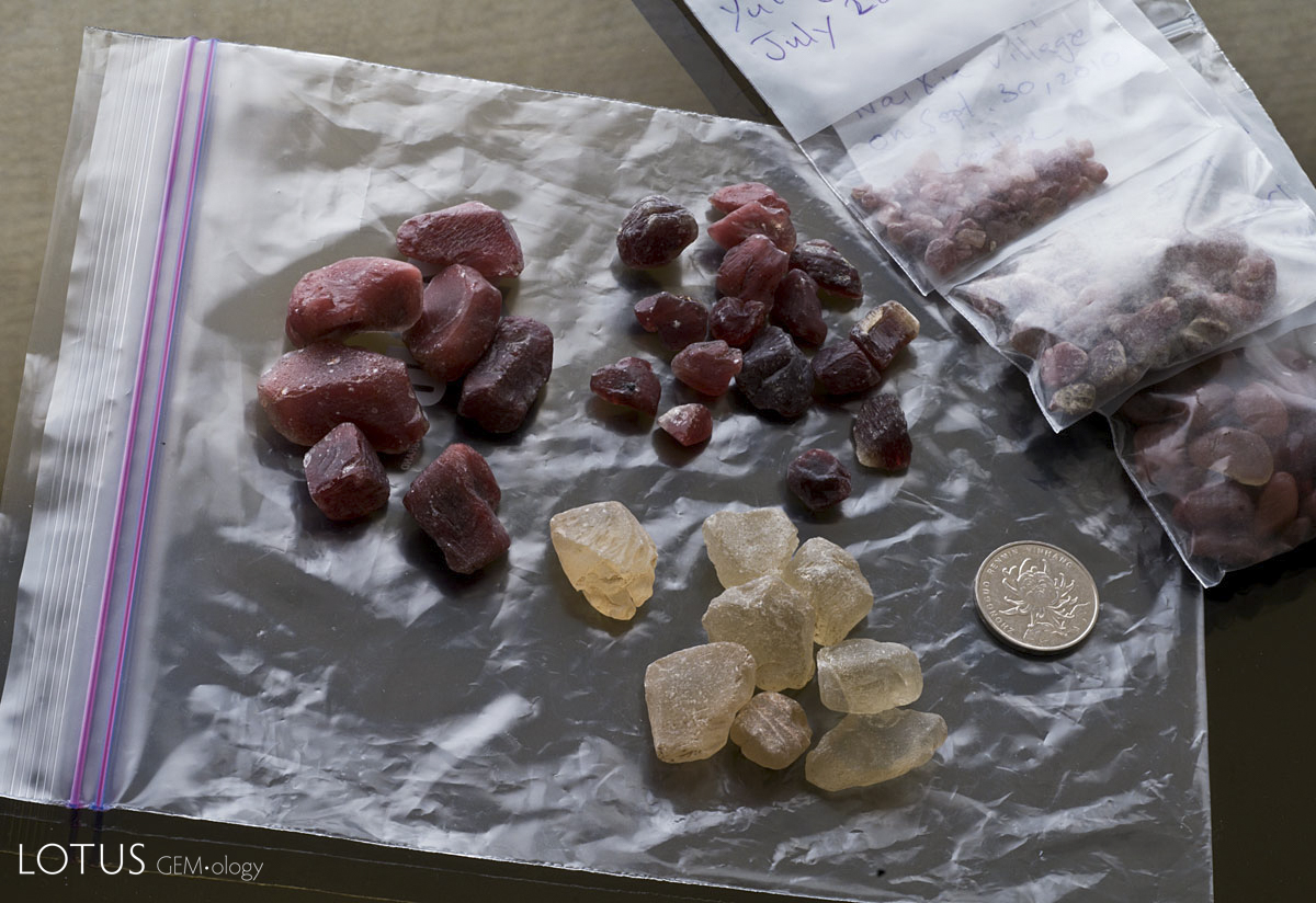 Figure 3. Pale yellow untreated andesine said to come from Inner Mongolia, flanked by two lots of deep red treated andesine. The three bags of rough on the right are natural Tibetan andesine. Untreated and treated Inner Mongolian andesines courtesy of Marco Cheung of Litto Gems. Photo: Wimon Manorotkul
