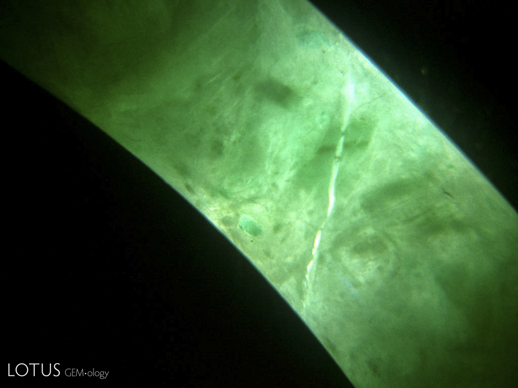 Figure 34. This jadeite bangle bracelet was broken and glued back together. The cement layer appears as a colorless area running vertically across the center of the photo. Under UV light, the glue in this piece fluoresced blue. Photo &copy; Richard W. Hughes