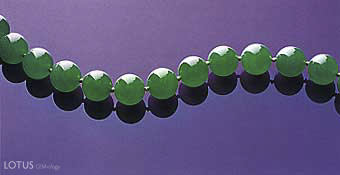 Figure 25. Uniformity of a fine "emerald" green color, superb translucency, size, and symmetry all come together to produce the necklace known as the Doubly Fortunate. The 27 beads, which range from 15.09&ndash;15.84 mm, were all cut from the same piece of rough, a 1 kg portion of a much larger boulder. The name derived from the fact that the necklace's owners "doubled their fortunes" every time the boulder was cut (Christie's, 1997, p. 70). The necklace sold in 1997 for approximately US$9.3 million. Photo courtesy of and &copy; Christie's Hong Kong and Tino Hammid.